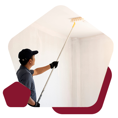 A person wearing a hat and gloves uses a long-handled roller to paint a ceiling white.