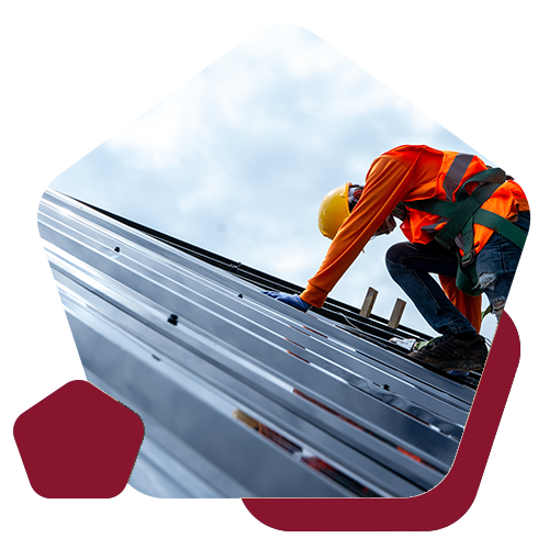 A worker in a yellow hard hat and safety harness installs metal roofing panels on a building.