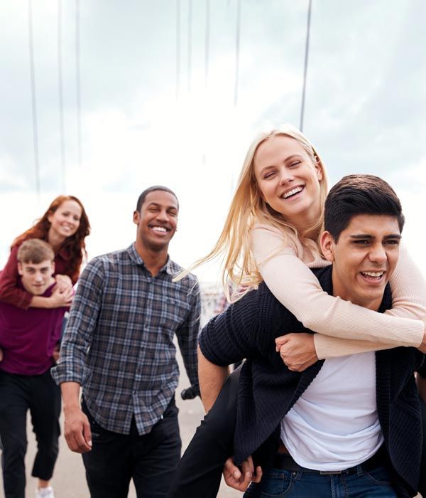 Friends walking outdoors, one man giving a woman a piggyback ride and both smiling