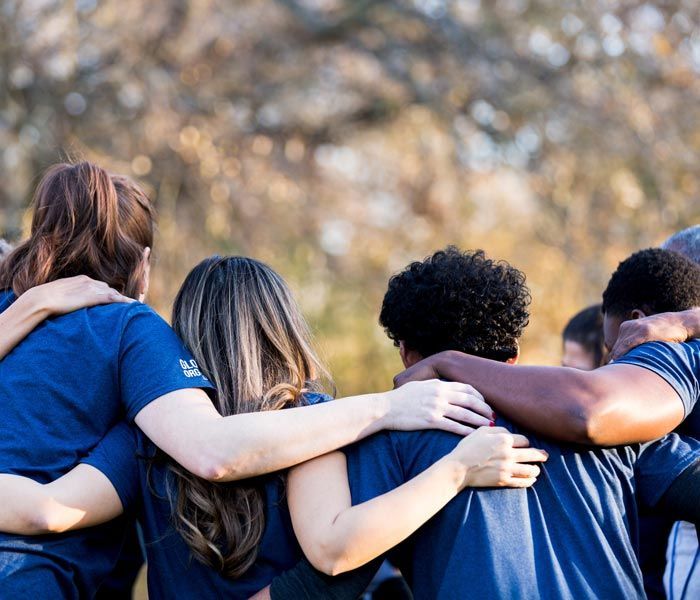 Group of people in blue shirts with arms around each other outdoors in a circle
