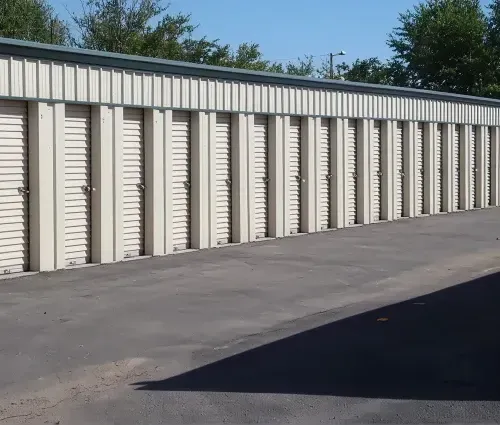 Row of beige storage unit doors beside an empty paved lot under a clear blue sky
