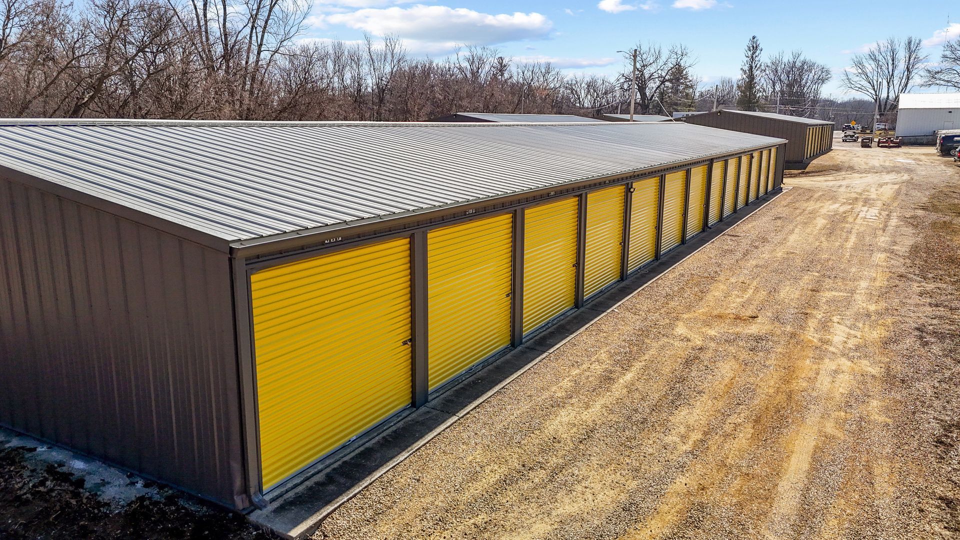 A row of storage units with yellow doors on a dirt road.