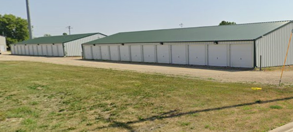 Storage units with white doors, green roofs, and a grassy foreground.