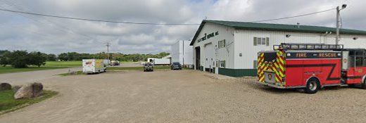 A red fire truck parked outside a white building with a green roof, on a gravel lot.