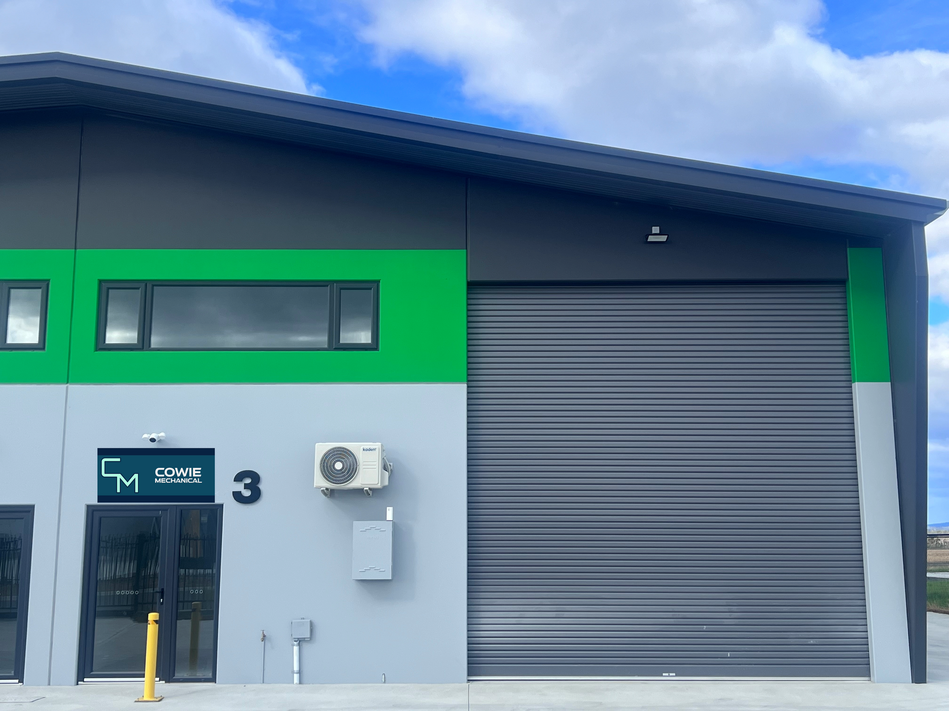 Exterior of a commercial building, with green, gray and black facade, closed garage door, and number 3.