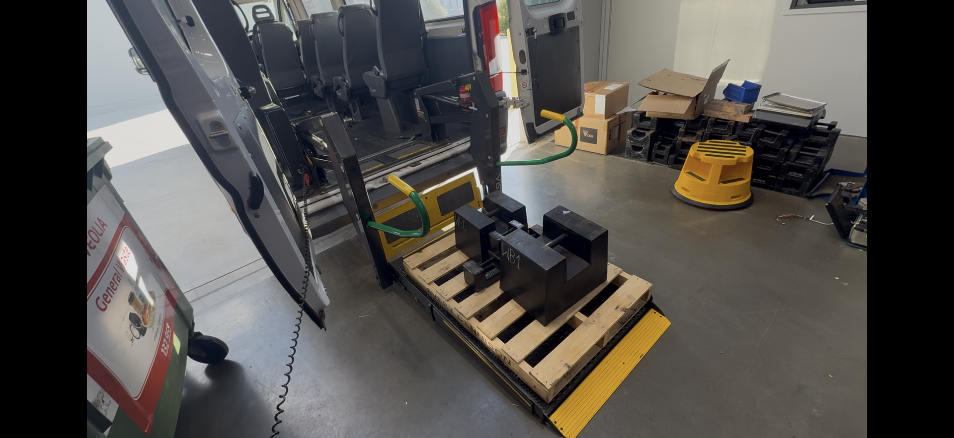 A loading dock with a pallet holding black boxes, near bus seating.