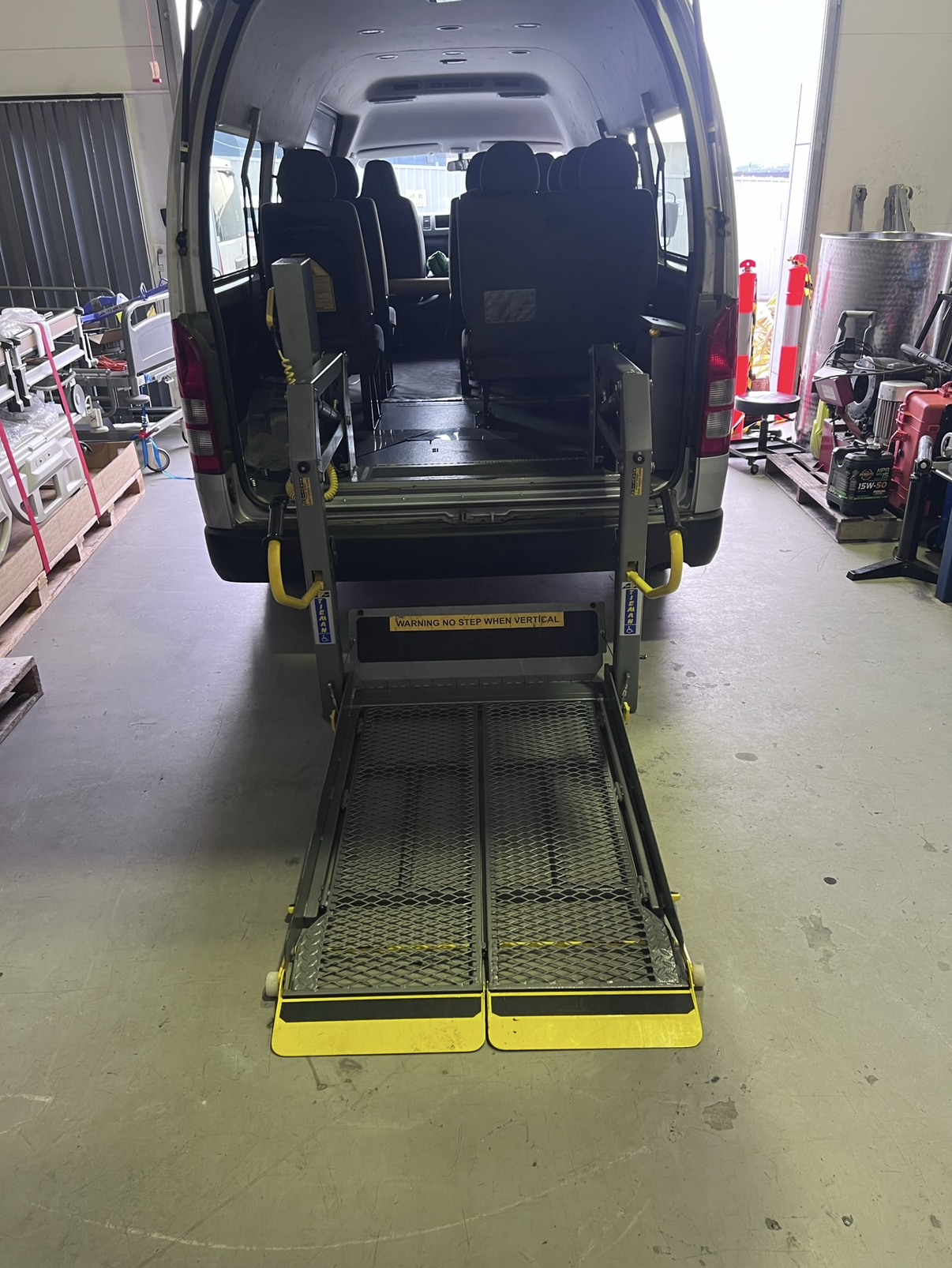 Wheelchair accessible van with deployed lift. Gray van, open rear doors, yellow lift platform extended.