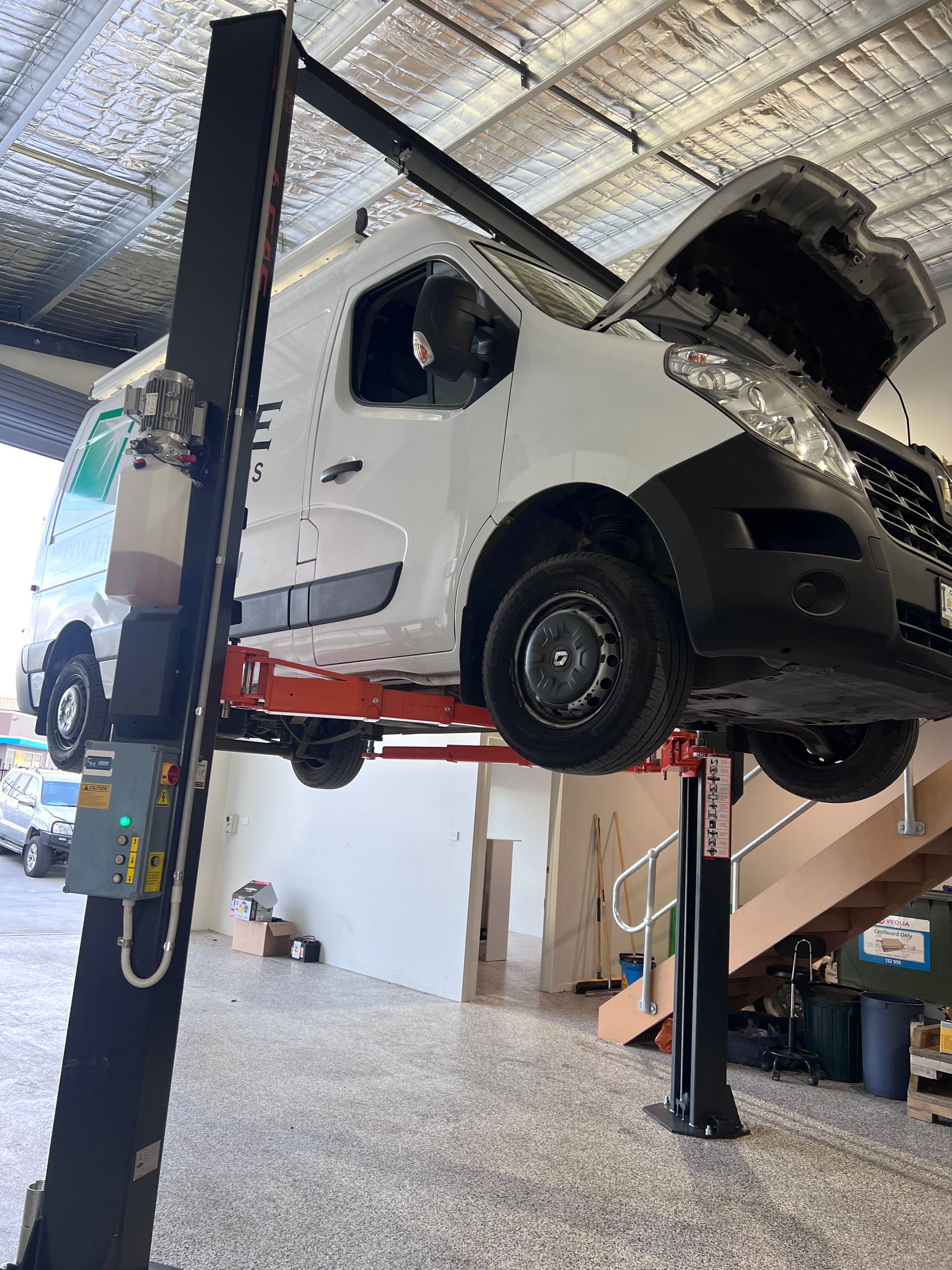 White van on a two-post car lift with hood open, in a garage.