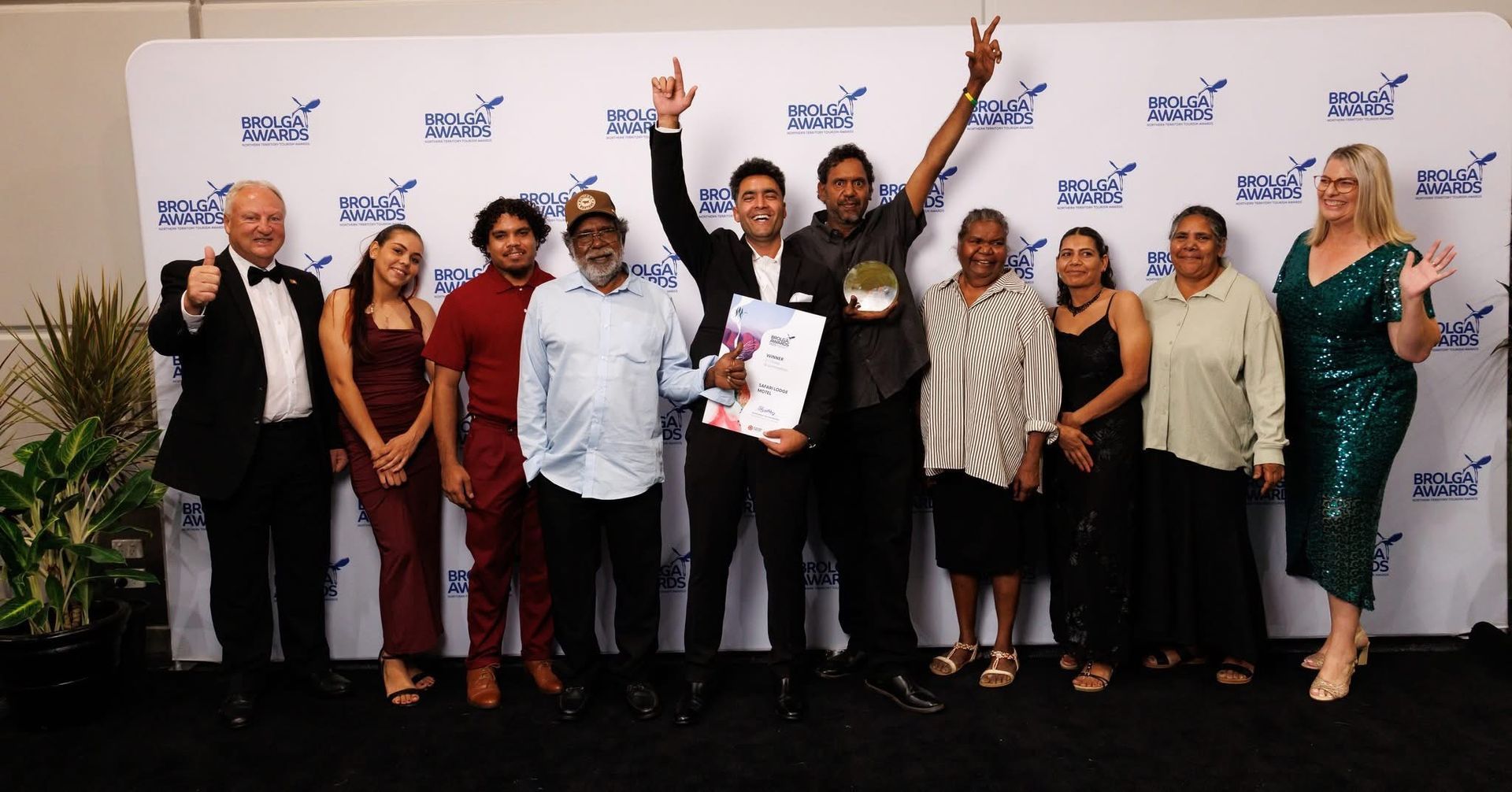 Group of people posing on a stage, with one person holding a certificate and two raising their arms in celebration.