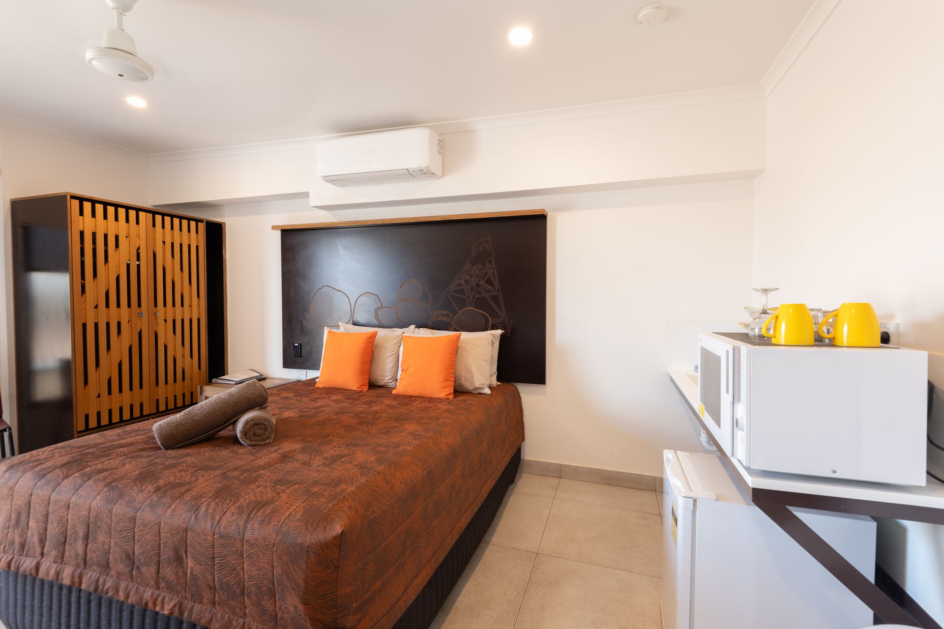 A small bedroom with a bed, wardrobe, and microwave, decorated with orange and brown tones.