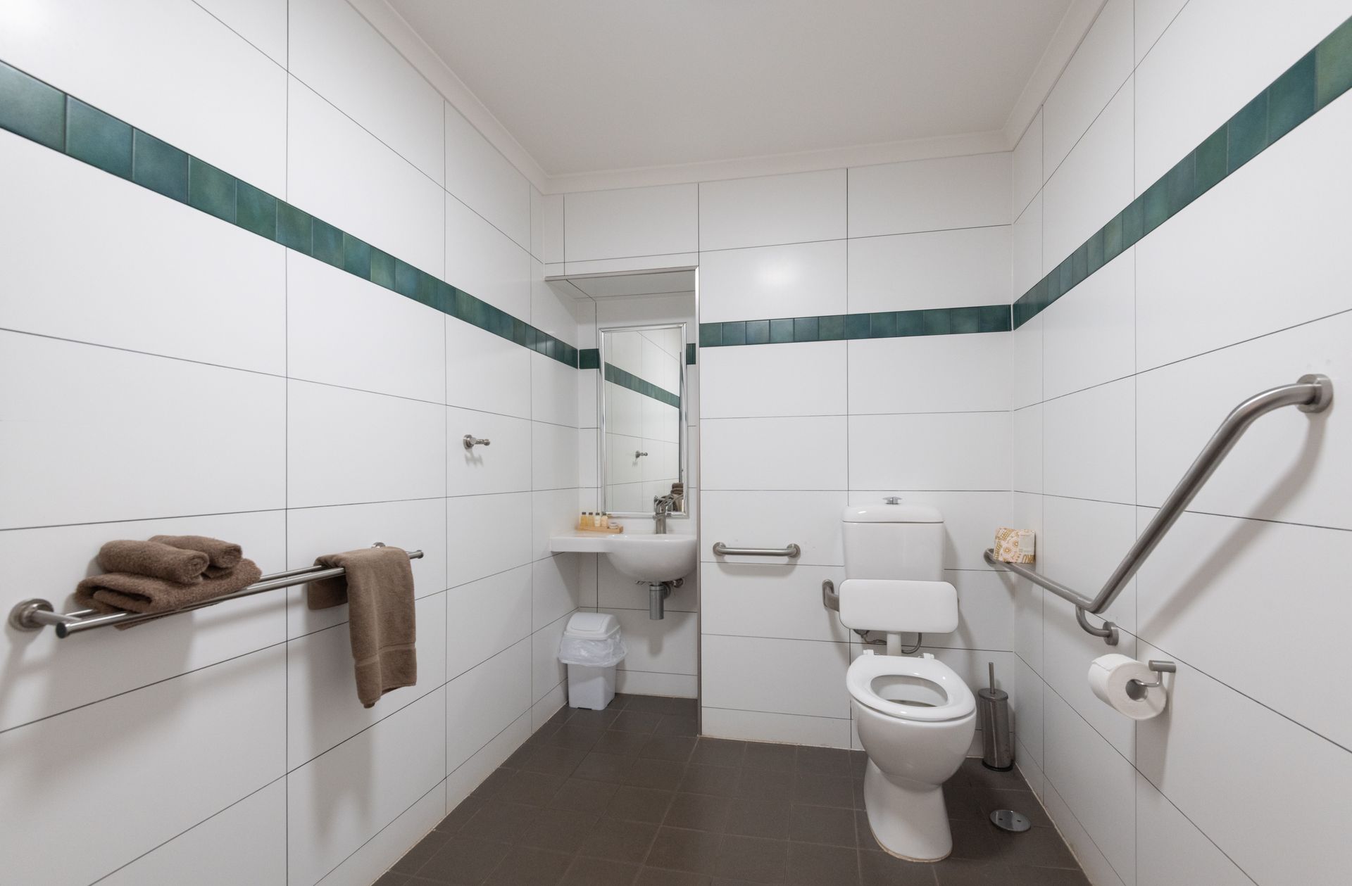 Accessible bathroom with white tiled walls, a toilet, sink, and grab bars. Includes a towel rack with towels.