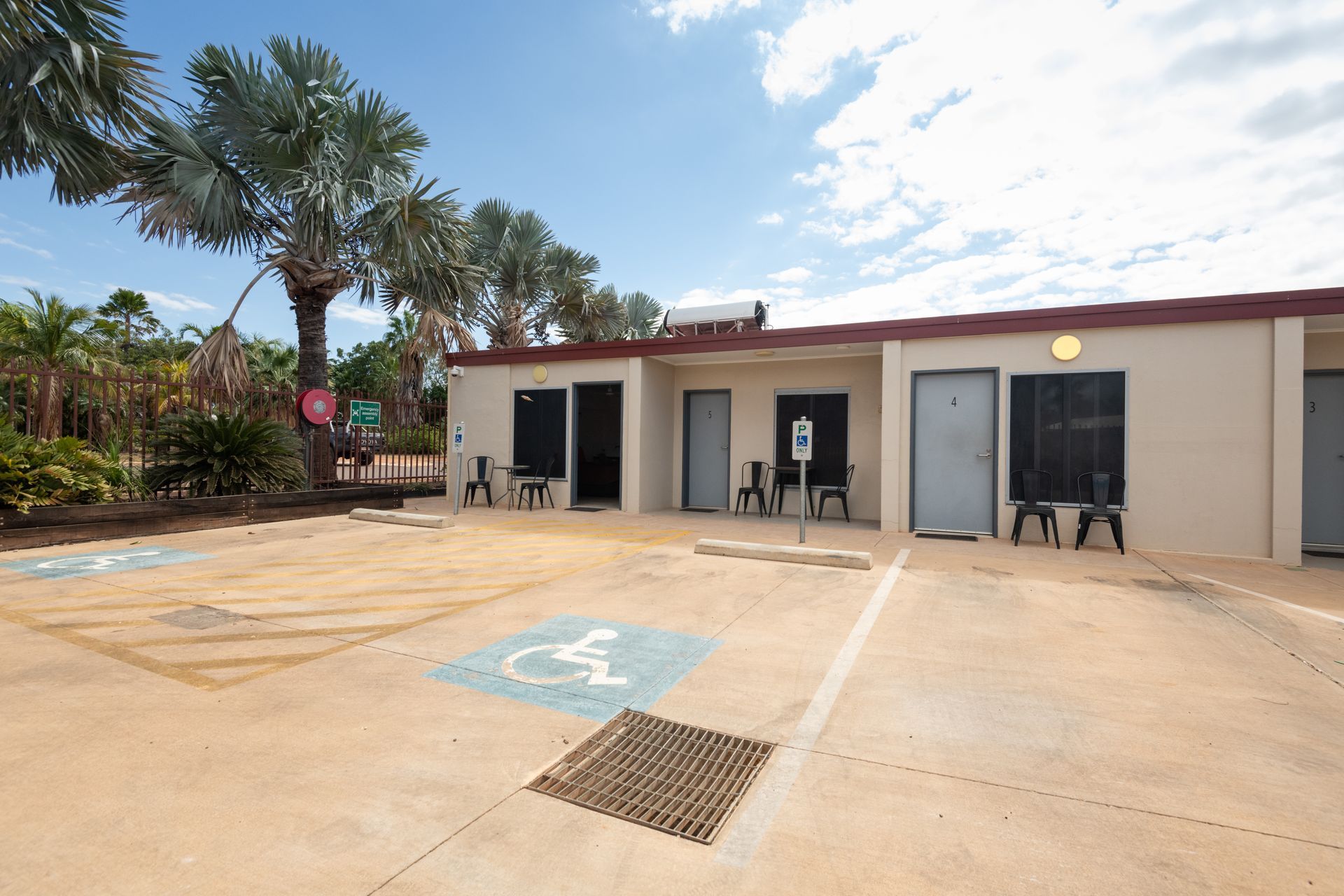 Exterior of a light-colored building with multiple entry doors, including an accessible parking space. Palm trees in the background.
