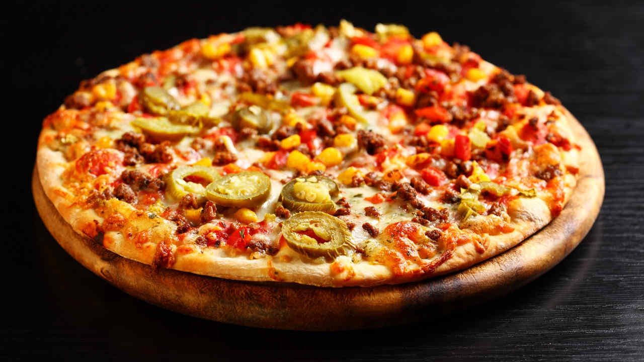 Pizza topped with meat, jalapenos, corn, and peppers on a wooden board.