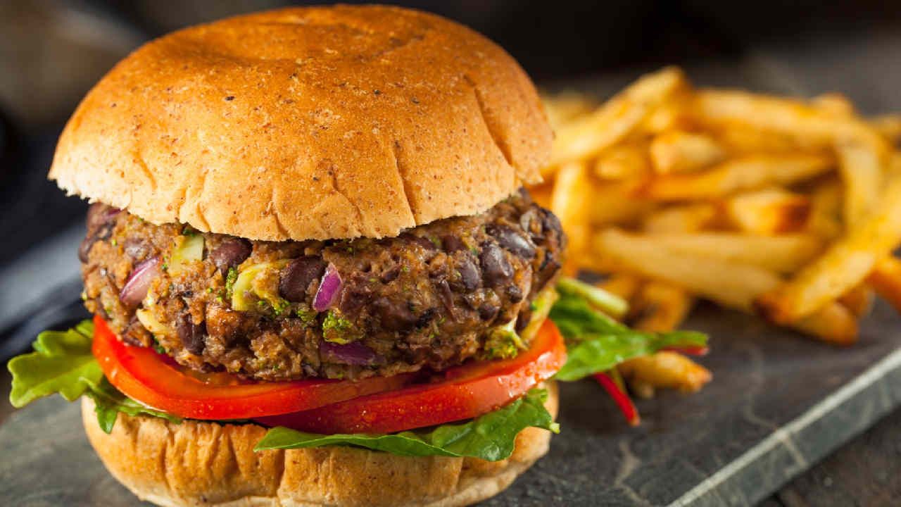 Black bean burger on a bun with tomato and lettuce, served with fries on a dark stone surface.