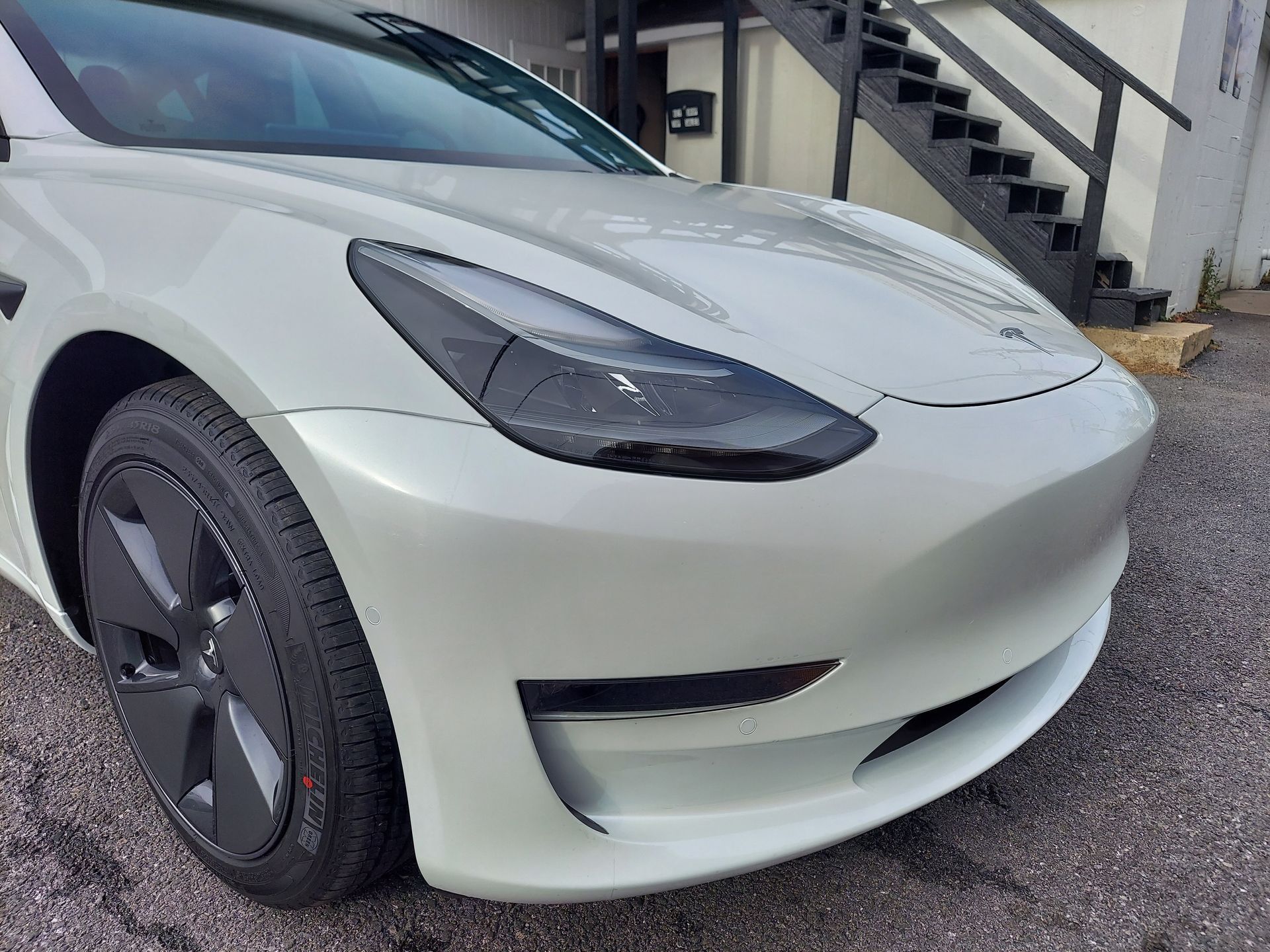 White Tesla Model 3 car parked outdoors, front view. Black tires, headlights and a black trim.