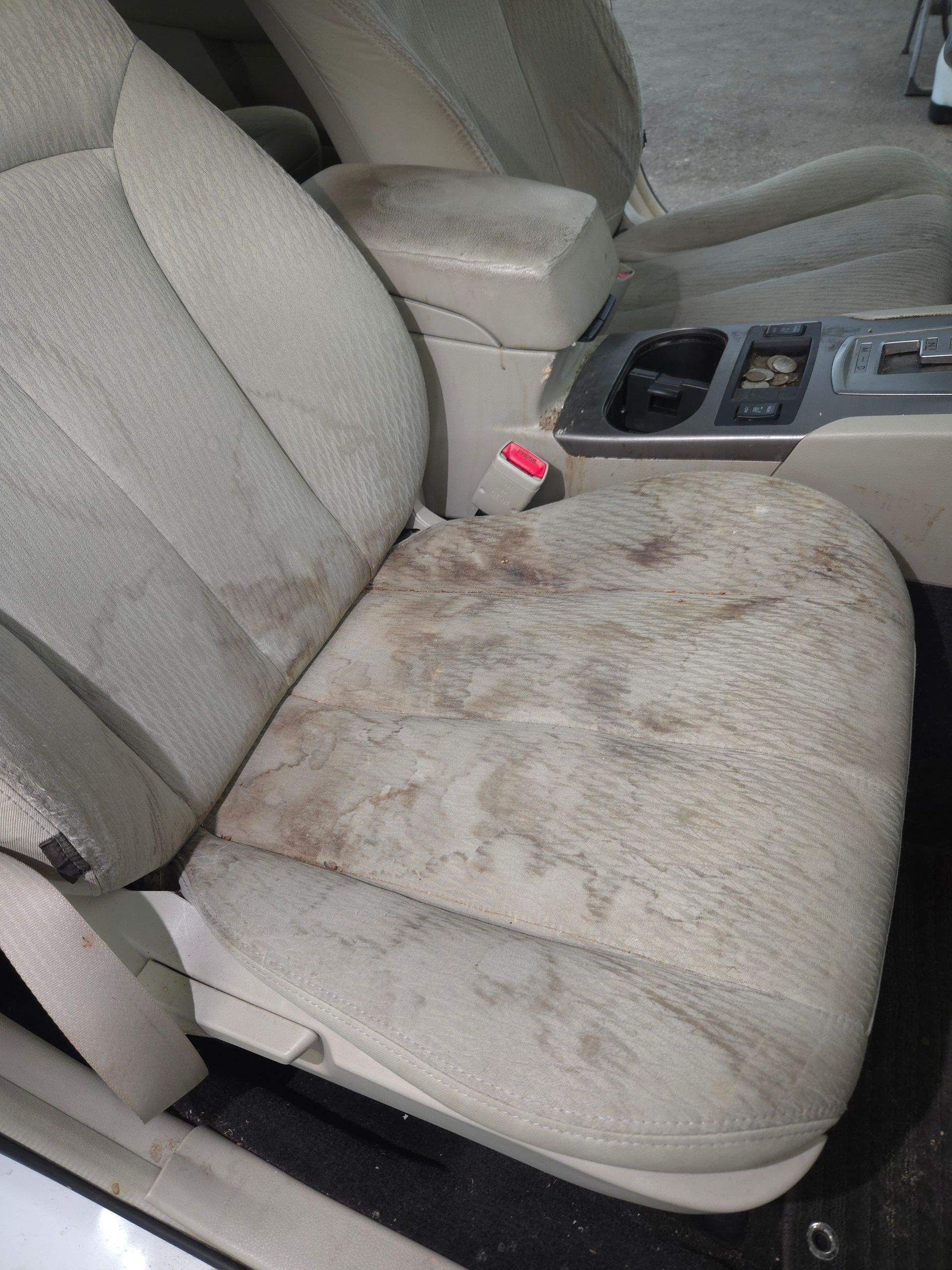 Beige car seat heavily stained with dark discoloration.