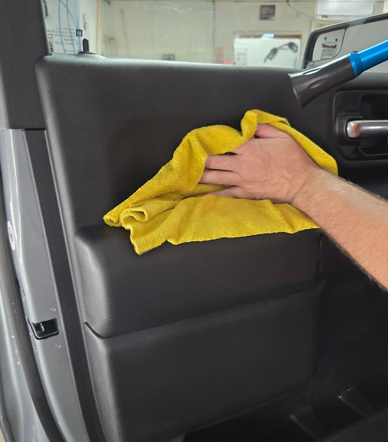 Person cleaning a black car door panel with a yellow cloth and vacuum.
