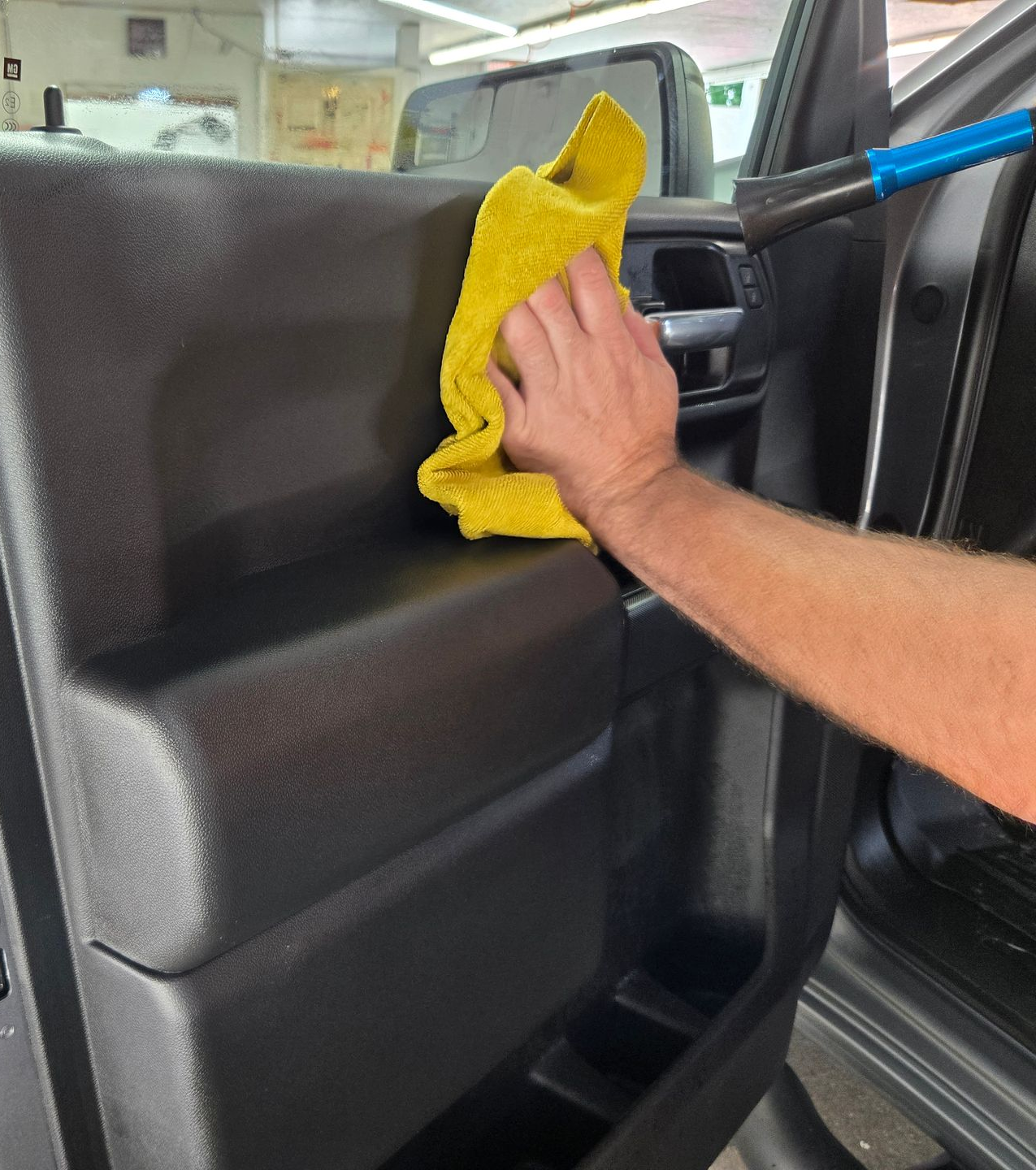 A person wearing a black glove vacuums a car's interior, cleaning the carpet.