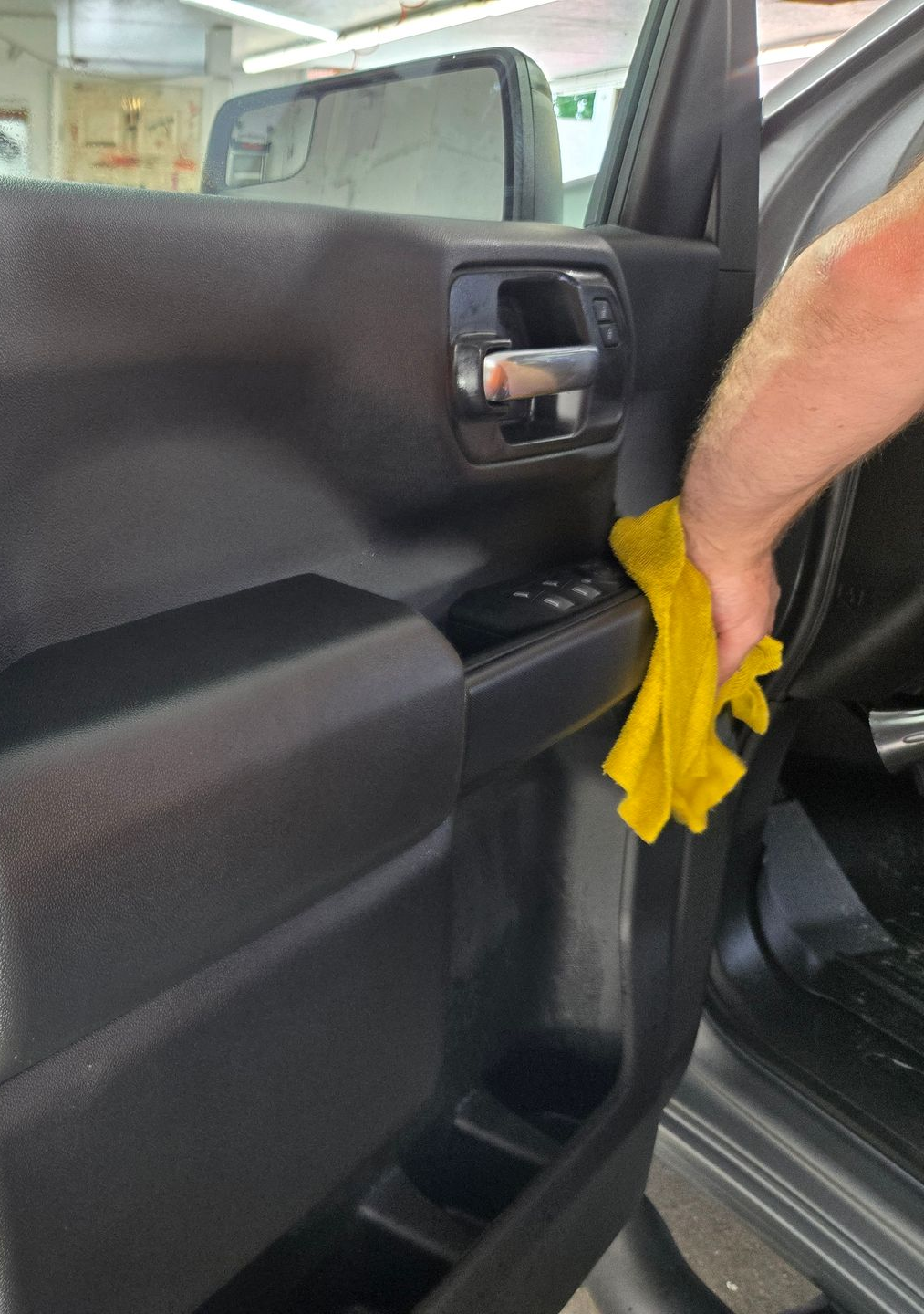 A person wearing black gloves cleans a car's air vent with a brush; interior detail.