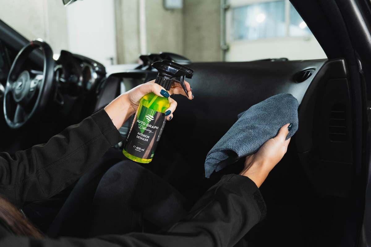 Person cleaning a car dashboard with spray bottle and cloth.