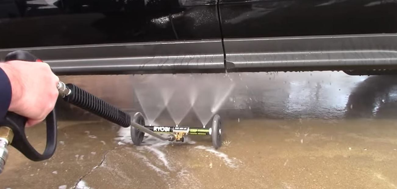 A person using a pressure washer to clean the undercarriage of a black vehicle.