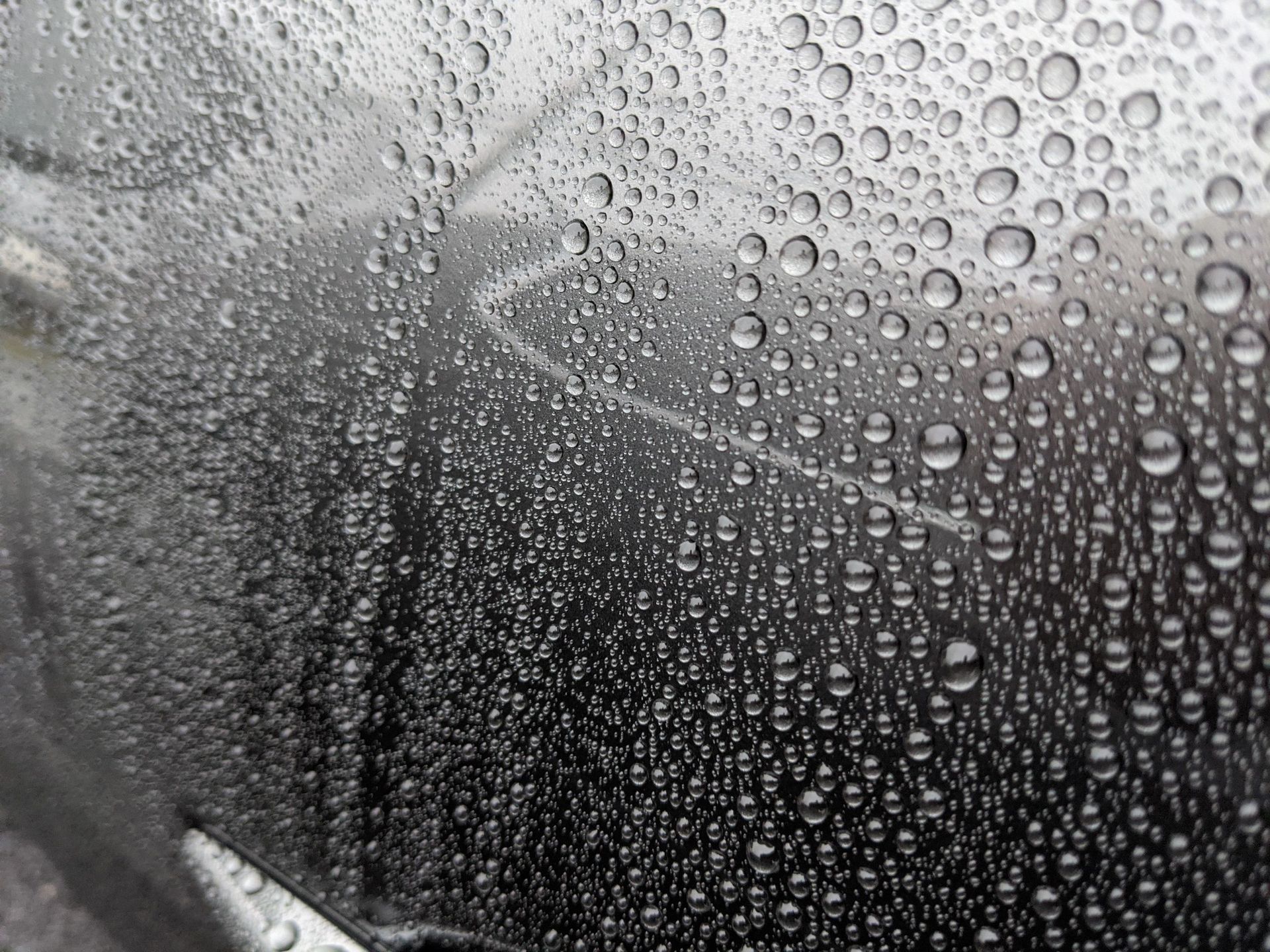 Raindrops on a windshield, obscuring a blurred road view.
