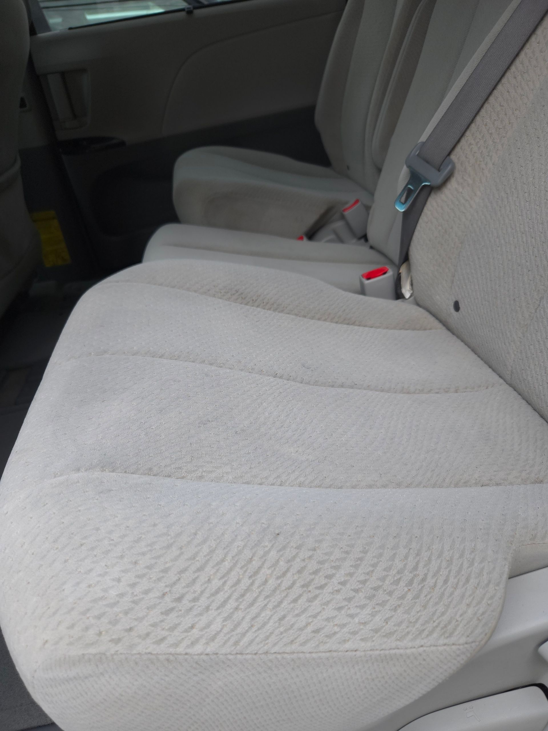 Beige car seat with fabric upholstery, showing wear.
