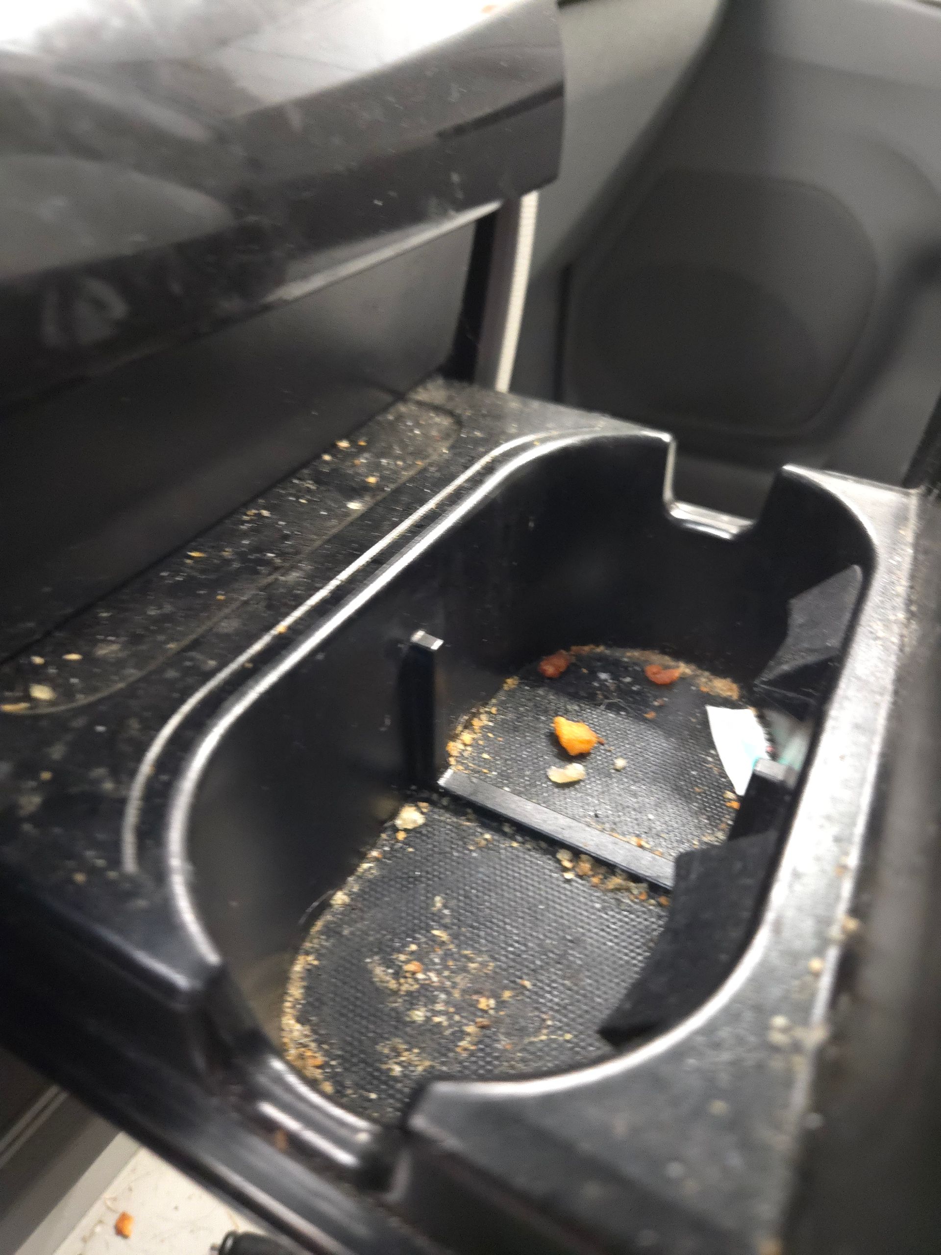 Dirty car cup holder with crumbs and debris.