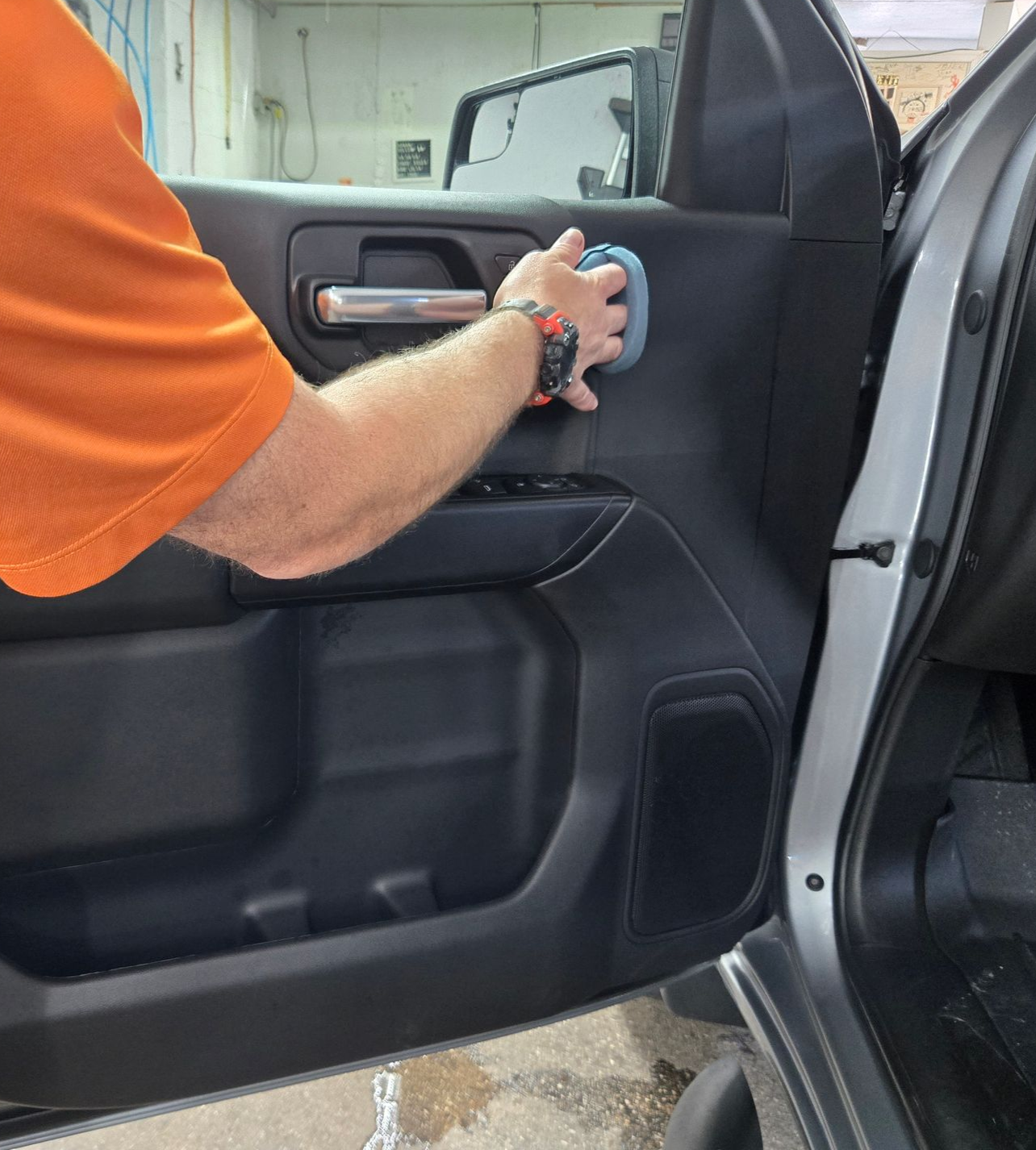 Person cleaning a car door interior with a blue sponge in an orange shirt.