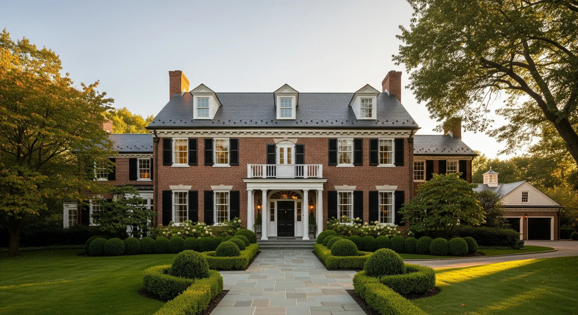 Large brick mansion with black shutters, dormers, and manicured lawn.
