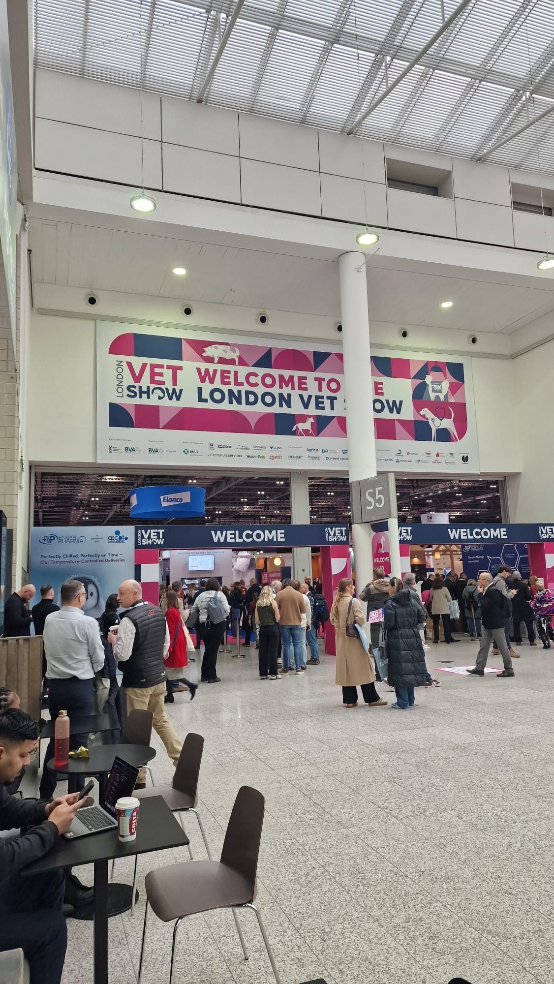 Crowded convention hall with a large “Welcome to London” banner and people queuing near vendor booths