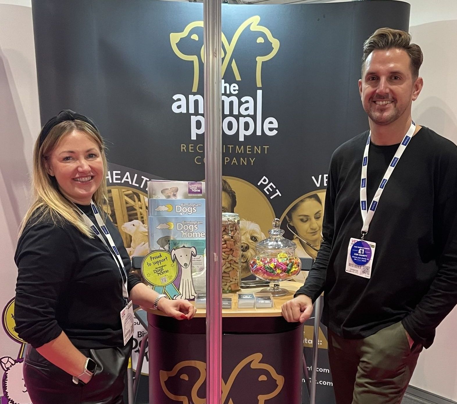 Two people stand by a display booth with clear jars and a black banner reading “animal people”