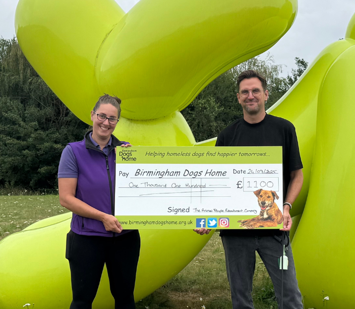 Two people holding a large ceremonial check in front of bright green balloon letters outdoors