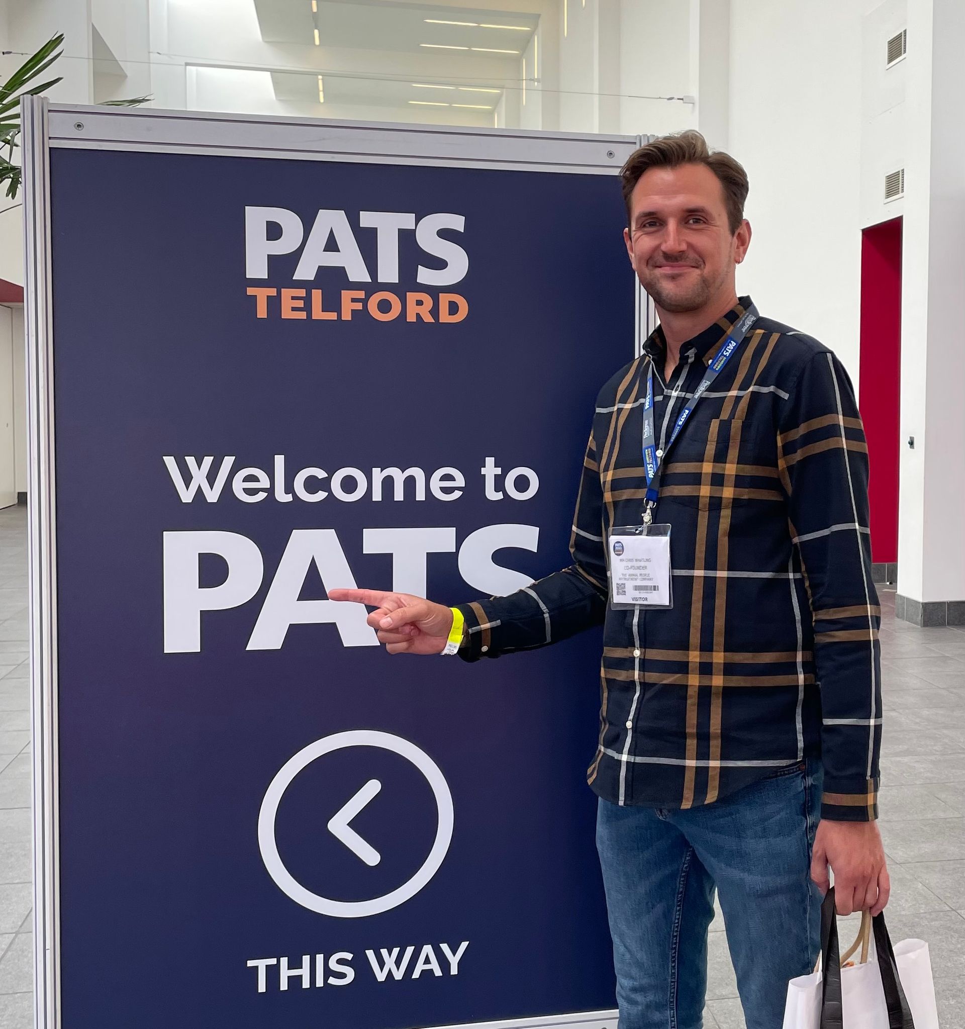 Man standing beside a PATS Telford welcome sign in a hallway, pointing to “This way” with a left arrow.