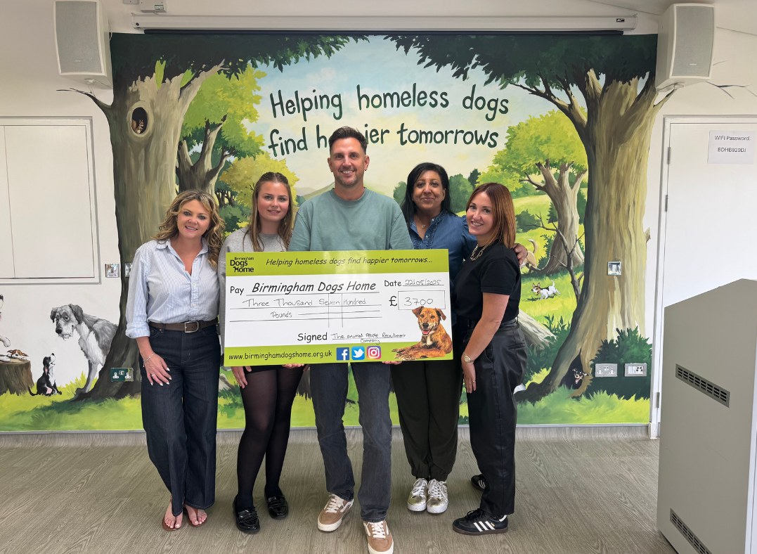 Four people hold a large check in front of a mural reading “Helping homeless dogs and their humans.”