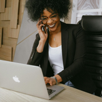 Woman smiling on a phone call beside a laptop in an office chair