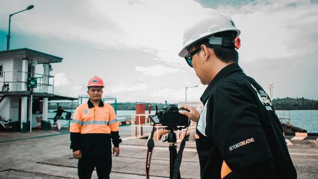 Photographer taking a portrait of a worker in safety gear at a harbor.