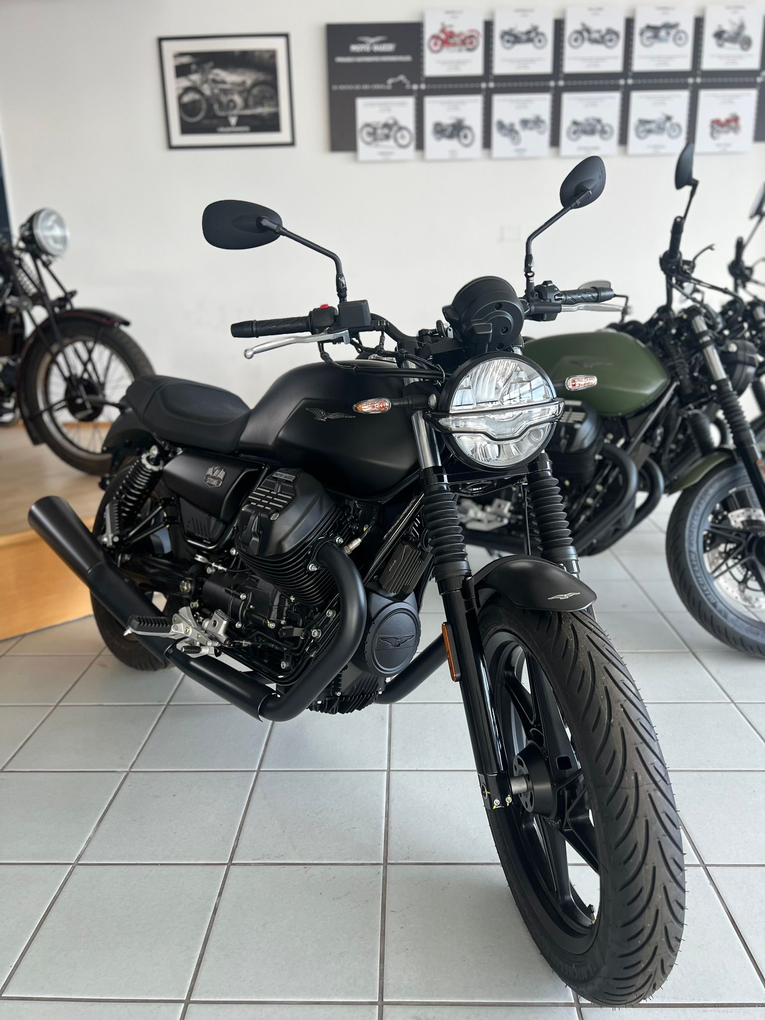 Una moto nera è parcheggiata in uno showroom accanto a una motocicletta verde.