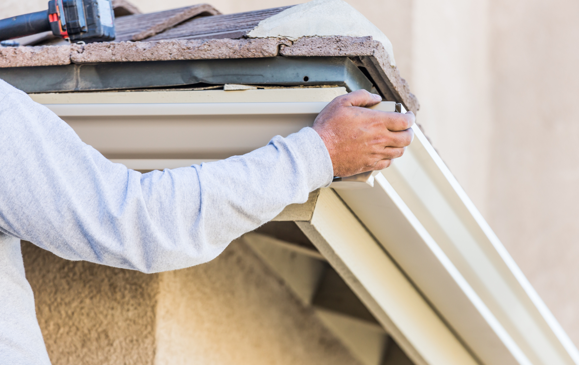 A man is installing a gutter on the side of a building.