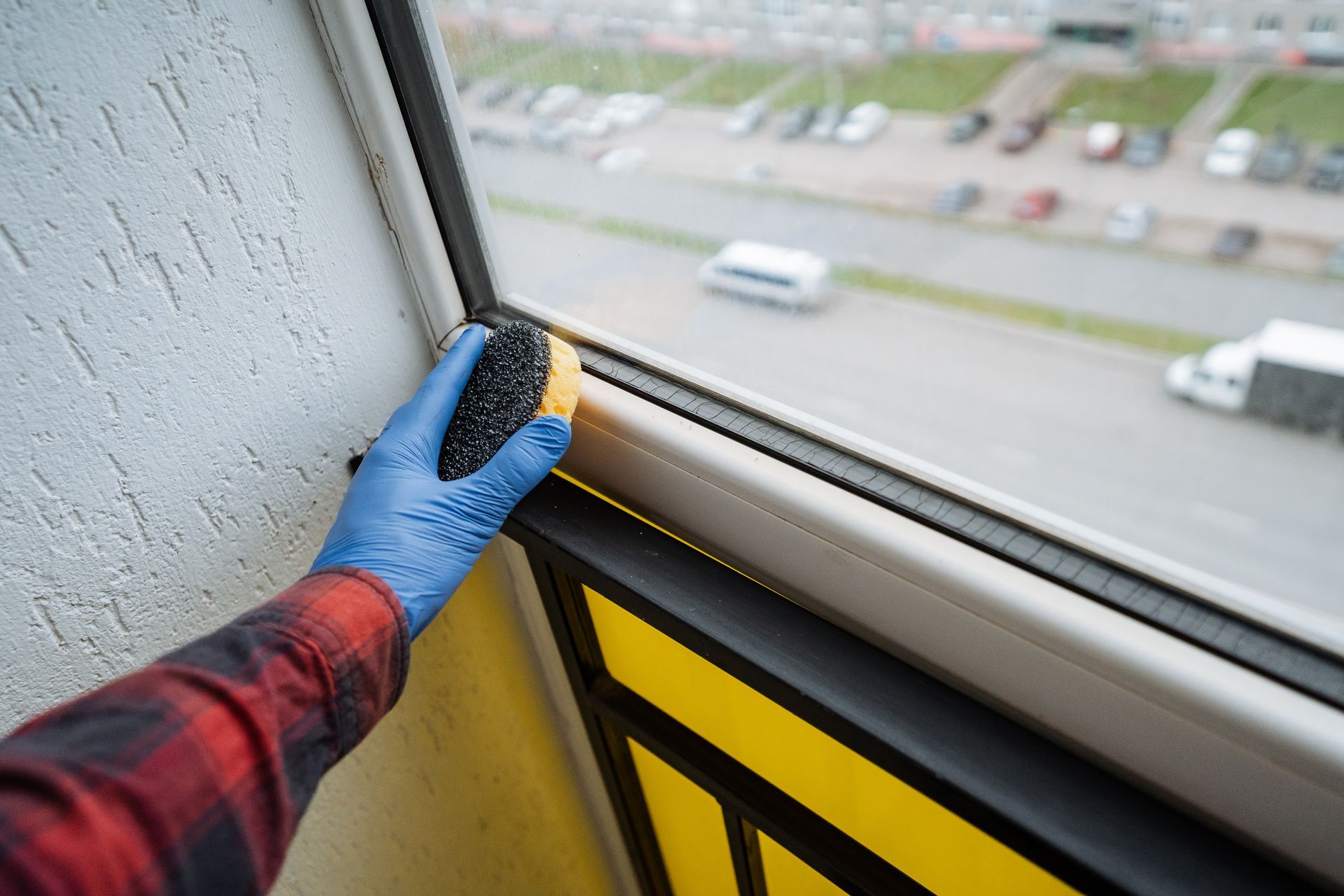 A gloved hand cleaning a windowsill with a view of passing traffic. A gloved hand cleaning a windowsill with a view of passing traffic.