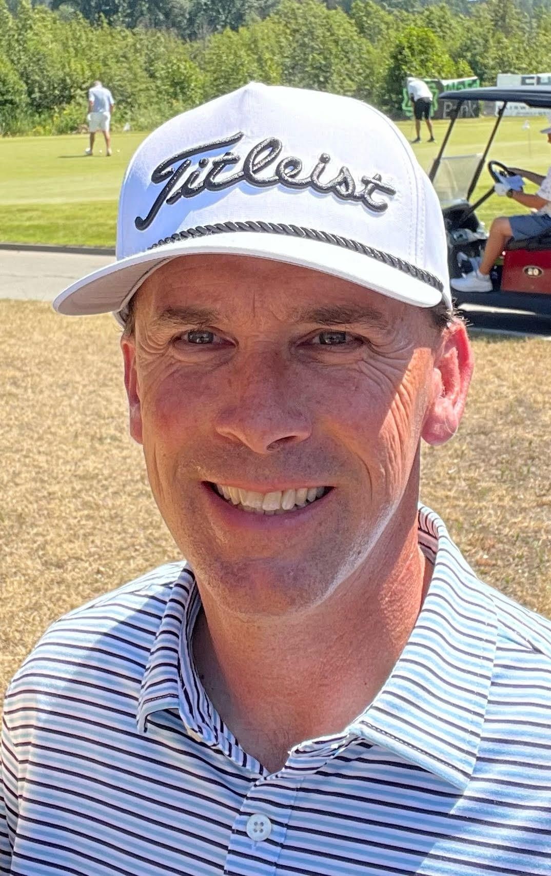 A man wearing a white hat and a striped shirt is smiling on a golf course.