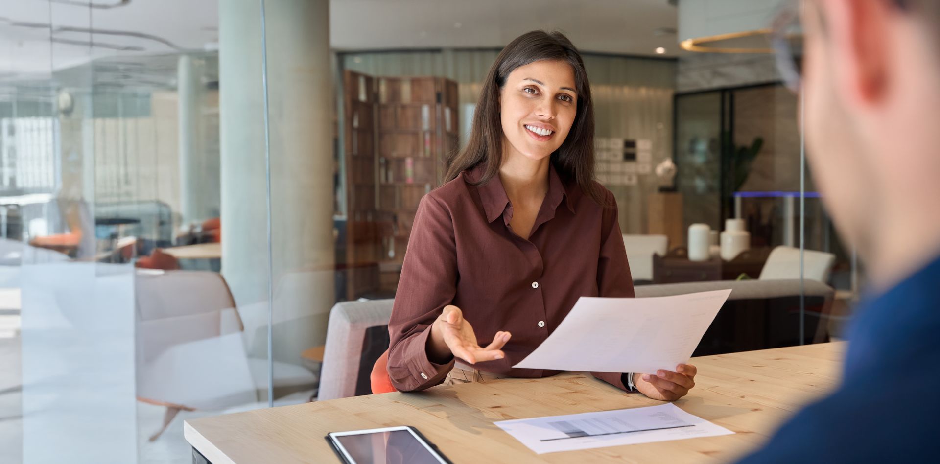 Woman holds a document and gestures while speaking to a person across the table.