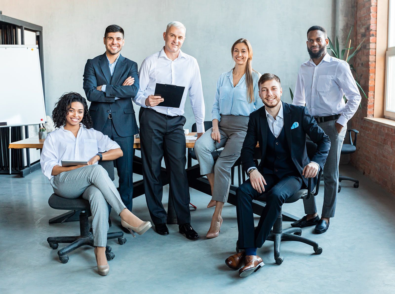 Six business professionals pose in a bright office, with two seated and four standing behind them.