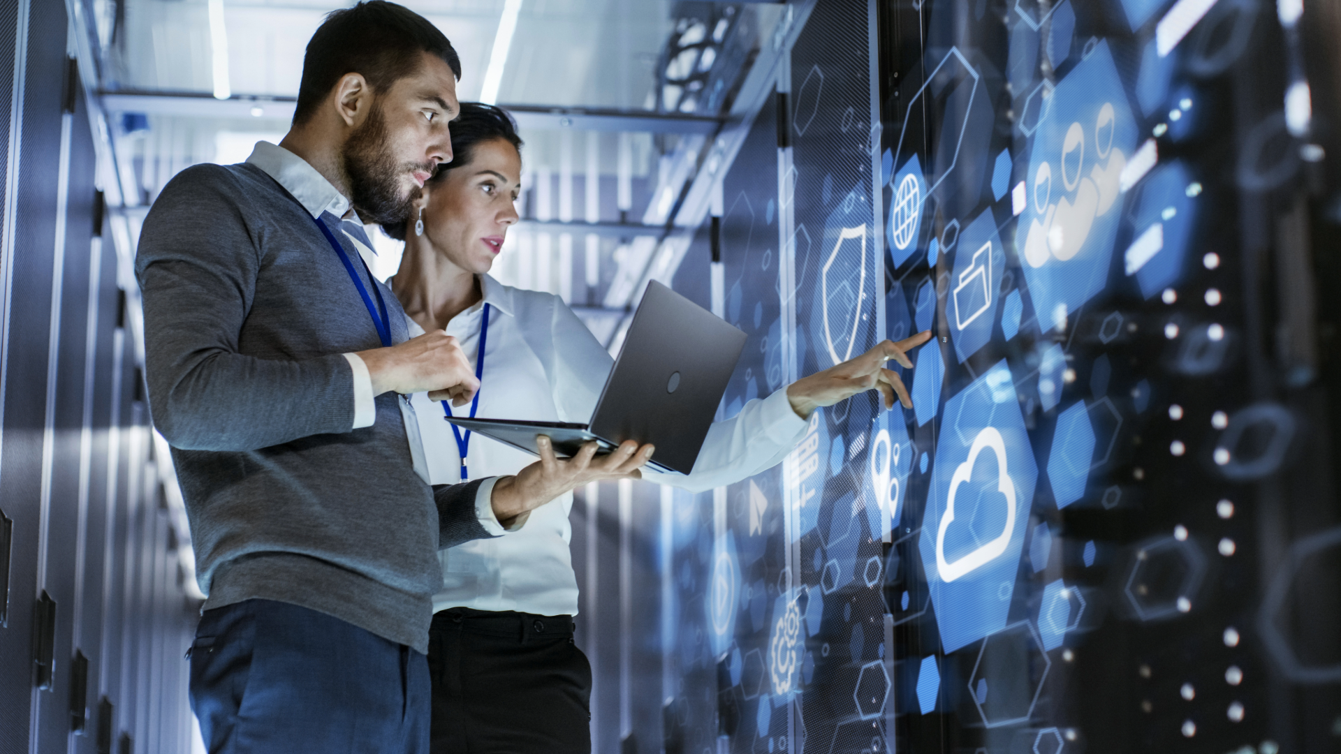 Two coworkers with a laptop reviewing glowing cloud data displays in a modern office.