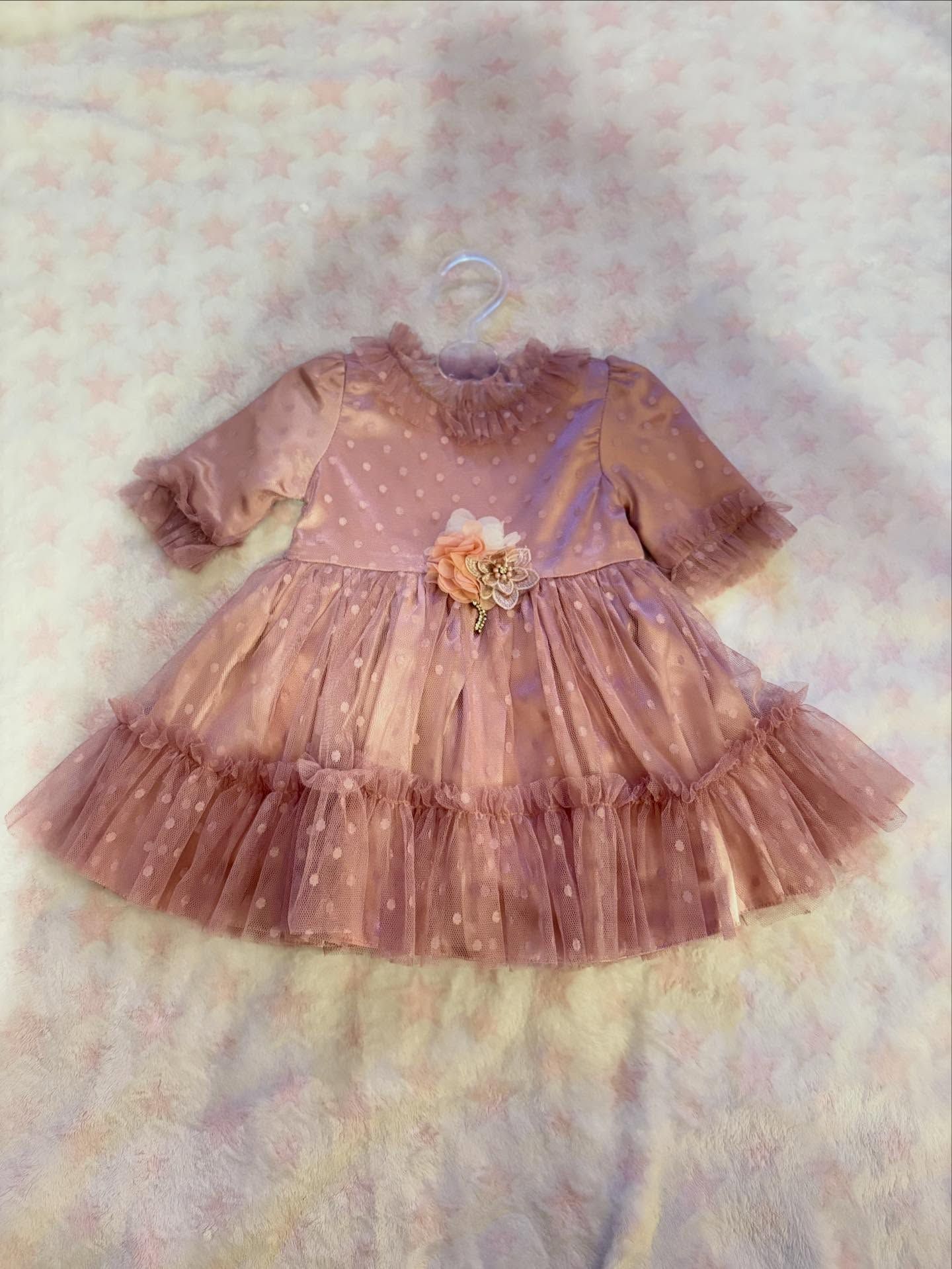 Abito rosa con decorazioni floreali, gonna in tulle e maniche a balze, appeso a una gruccia bianca.