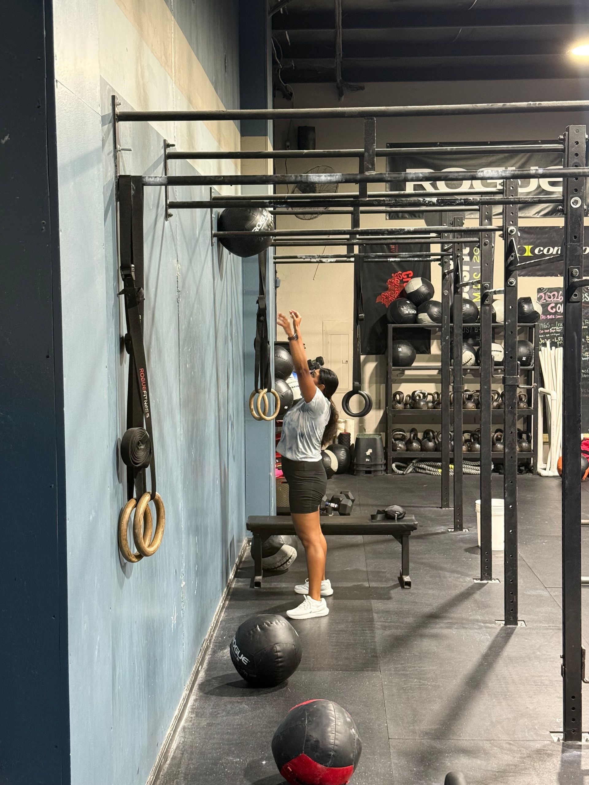 Person reaching up at a pull-up rig in a gym, with medicine balls on the floor.