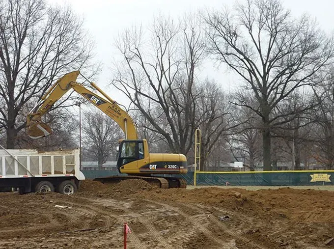 A yellow cat excavator is loading dirt into a dump truck