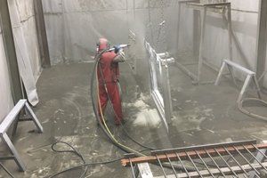 A man in a red suit is spray painting a piece of metal in a room.