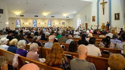 People seated in wooden church pews, many with heads bowed in quiet prayer.