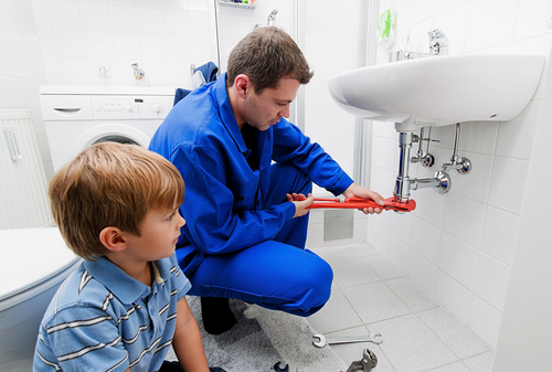 A1 Handyman technician performing bathroom sink plumbing repair with a child observing, showing family-friendly home service.